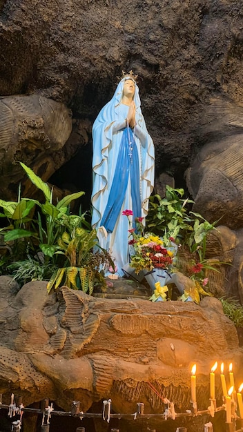 Statue der Heiligen Jungfrau Maria in der römisch-katholischen Kirche in der Höhle der Jungfrau Maria in einer Felsenhöhlenkapelle Katholische Kirche mit tropischen Blumen in Asien
