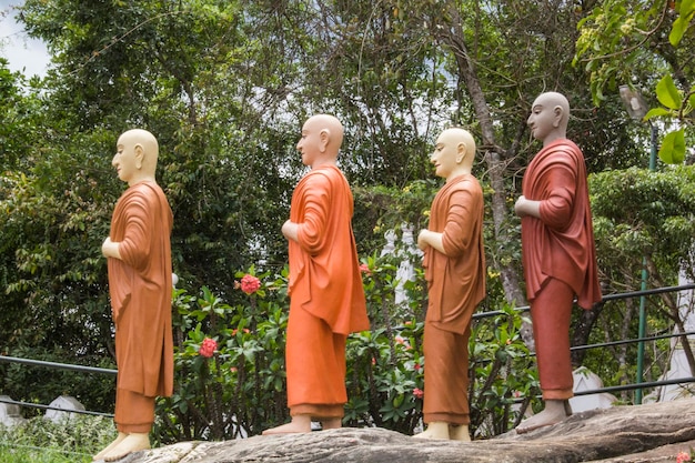 Statuen von Buddhas auf einem Felsen vor einem Baum.