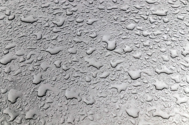 Staubige Wassertropfen auf dem Glas und der Motorhaube eines Autos