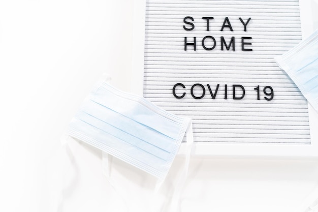 STAY HOME e COVID-19 assinam no quadro de mensagens com uma máscara médica azul.