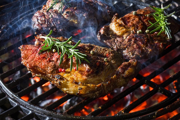 Steak auf dem Grill, gewürzt mit frischem Rosmarin Brennende Holzkohle hält gekochtes Fleisch warm Appetitlich gegrilltes Gericht Nahaufnahme selektiver Fokus