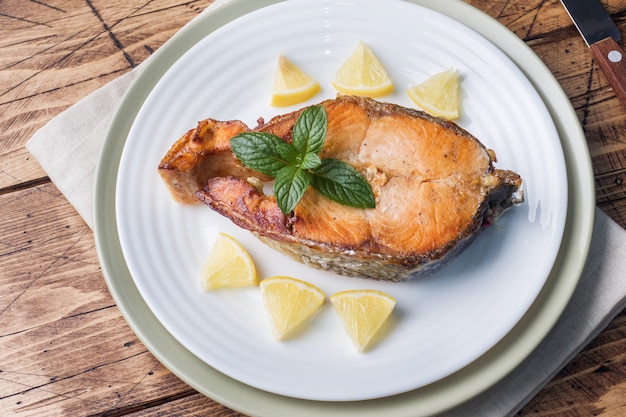Steak gebackener Fischlachs auf einer Platte mit Zitrone. Holztisch.