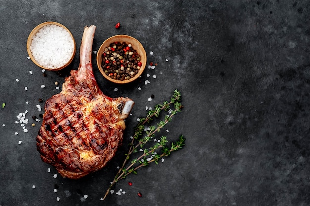 Steak - gegrillter Rindfleisch-Tomahawk mit Gewürzen, Thymian auf Steinhintergrund. mit Kopierplatz für Ihren Text