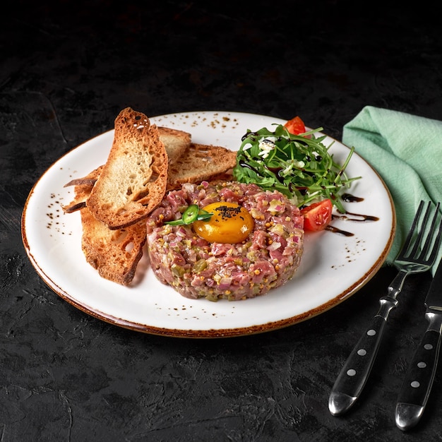 Steak Tartar mit Toastbrot serviert auf schwarzem Hintergrund. Vorspeise oder Snack. Speisekarte