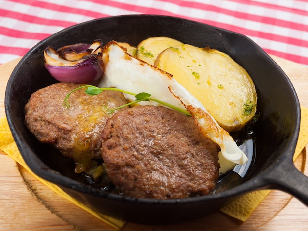 Steaks in einer Pfanne mit Kartoffeln und Zwiebeln