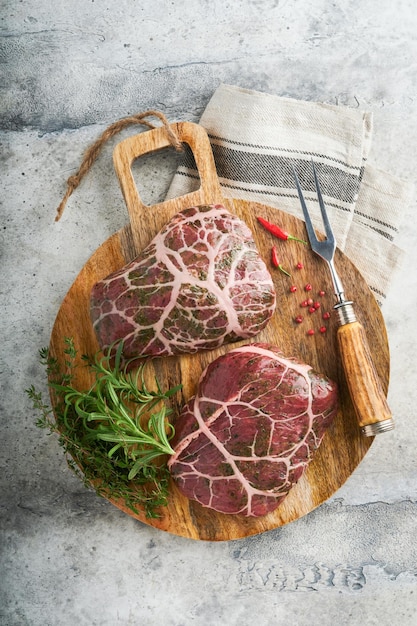 Steaks roh Rohes Cowboysteak marmoriertes Rindfleisch mit Gewürzen Rosmarin und Pfeffer auf altem Holzbrett auf altem grauem Schiefertisch Hintergrund Draufsicht Mock up