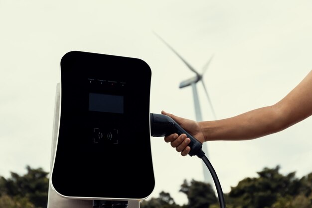 Stecken Sie den Stecker von Hand in das EV mit progressiver natürlicher Landschaft und Windturbine