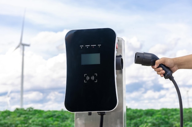 Stecken Sie den Stecker von Hand in das EV mit progressiver natürlicher Landschaft und Windturbine