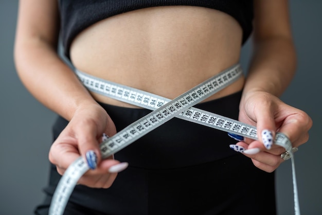 Stehende Fitnessfrau, die ihre Taille mit einem Band mit Zahlen misst