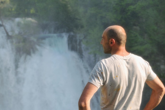 Stehender Mann mit weit geöffneten Armen mit Wasserfällen im Hintergrund, der Frische, gesunden Lebensstil und Erfolgskonzept darstellt