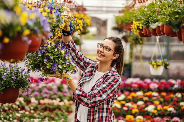 Stehender und hängender Topf des jungen lächelnden weiblichen Kindergartengartens mit Blumen.