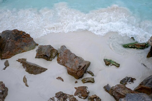 Steine am Strand und blaue Welle mit Meeresschaum auf goldenem Sand
