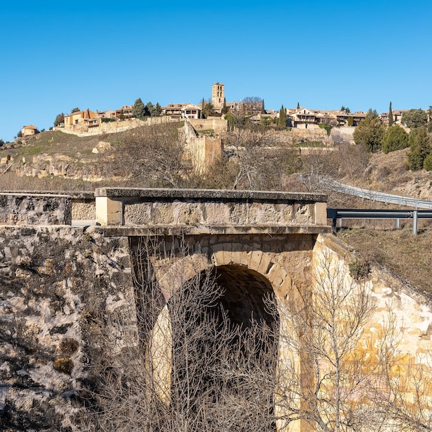 Steinerne Brücke über den Fluss, der am mittelalterlichen Dorf Pedraza in den Feldern von Kastilien-Spanien vorbeiführt