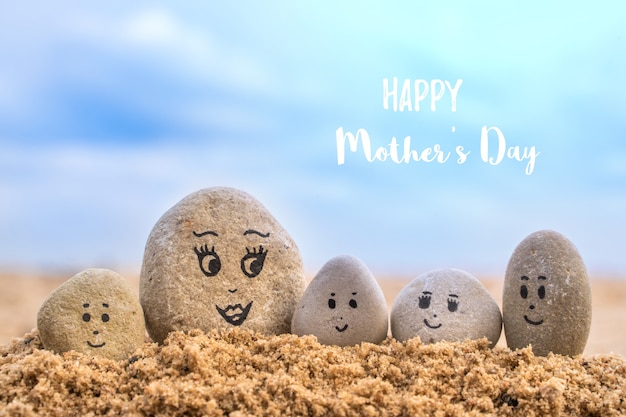 Steingruppe mit gezeichneten Gesichtern im Sand. Mutter und ihre Kinder. Glückliche Konzeptkarte zum Muttertag.