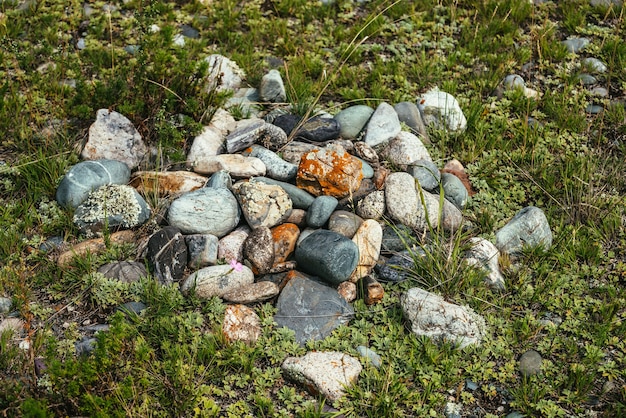 Steinhaufen mit Flechten und Moos auf grünem Gras. Kunstnaturhintergrund mit vielen Steinen auf dem Boden. Altaier heidnischer Friedhof. Alte heidnische Grabstätte der Altaier. Heidnischer Ritus im Altai. Haufen Steine.