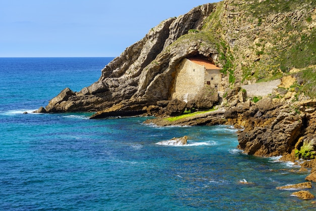 Steinhaus versteckt zwischen den Felsen auf einer Klippe vom Meer, Santander, Spanien
