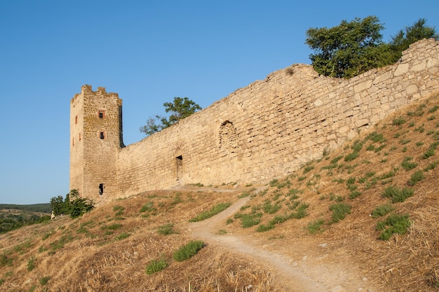 Steinturm einer alten Festung mit angrenzenden Felswänden auf blauem Himmelshintergrund