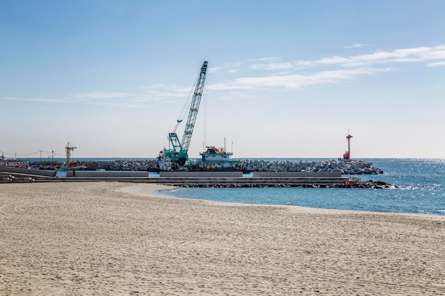 Steinwellenbrecher am Meer mit Sandstrand mit Baumaschinen