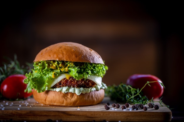 Stellen Sie knusprigen Hühnerburger mit Käse, Salat, Tomate und Soße auf hölzernem Hintergrund her