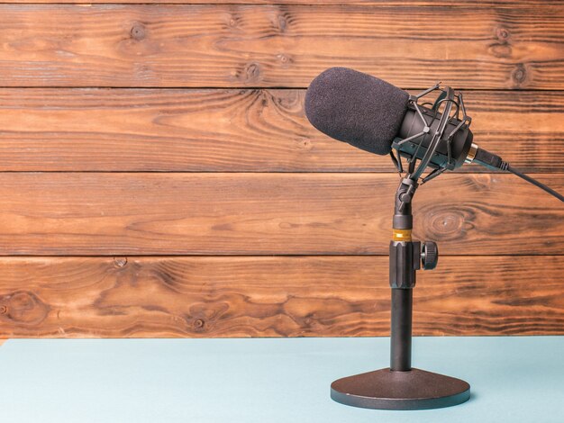 Stellen Sie sich mit einem modernen Mikrofon auf einen blauen Tisch auf einer Holzoberfläche