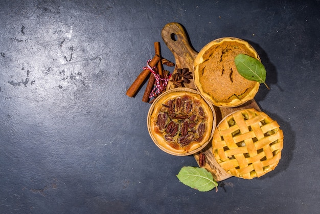 Stellen Sie verschiedene Herbstkuchen ein. Pekannuss-, Apfel-, Kürbis-kleine Tortenkuchen und Torten auf konkretem Hintergrund mit hellem Sonnenlicht, Draufsicht der dunklen Schatten