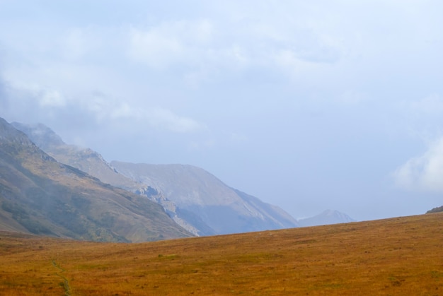 Steppenplateau, Almwiese im Herbst mit einem nebligen Grat in der Ferne