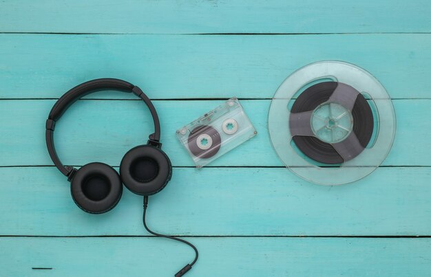Stereokopfhörer und magnetische Audiospule, Audiokassette auf blauem Holzhintergrund. Ansicht von oben
