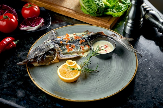 Sterlet assado no forno com molho branco e caviar vermelho, servido em um prato cinza sobre uma mesa de mármore escuro. Comida do restaurante. Frutos do mar