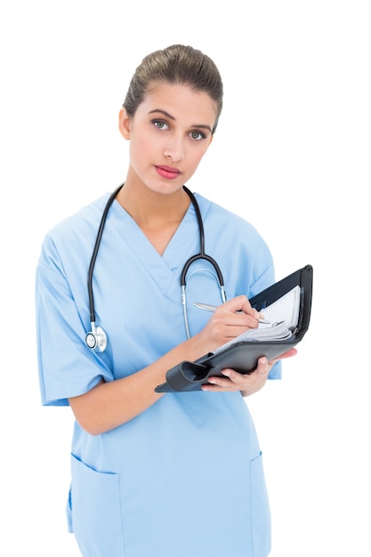Stern enfermera de cabello castaño en matorrales azules llenando una agenda