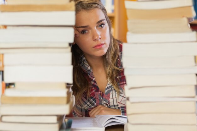 Stern estudante bonito estudando entre pilhas de livros