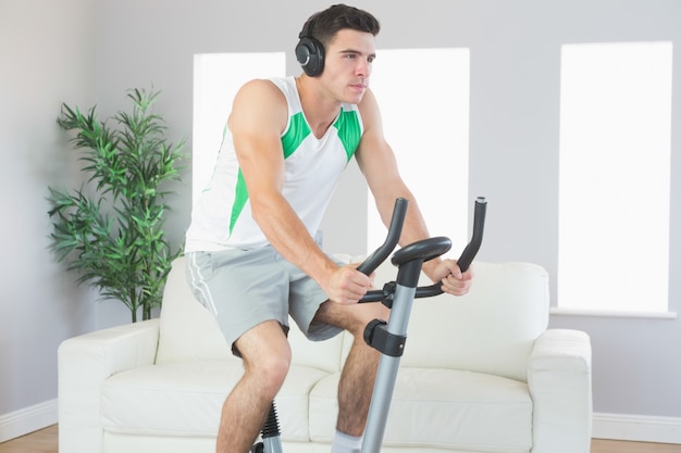 Stern homem bonito treinando na bicicleta de exercício ouvindo música