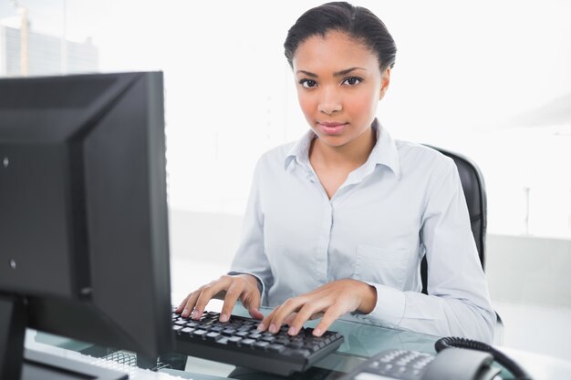 Foto stern jovem mulher de negócios de cabelos escuros digitando no computador