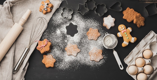 Sternförmige gebackene Lebkuchenplätzchen, bestreut mit Puderzucker auf einem schwarzen Tisch, Draufsicht