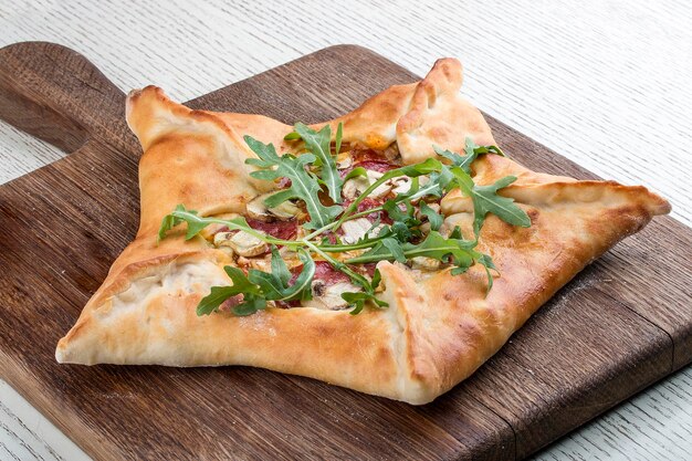 Foto sternförmige pizza mit schinken und rucola auf einem holzbrett