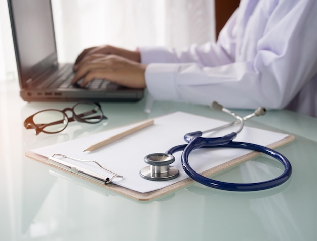 Stethoskop auf dem Tisch und ein Arzt, der am Laptop für Gesundheits- und Krankenhauskonzepte arbeitet