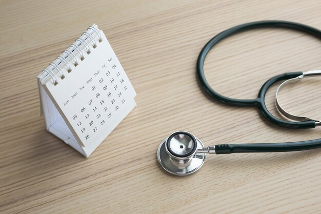 Stethoskop mit Kalenderseitendatum auf Holztischhintergrund Arzttermin medizinisches Konzept