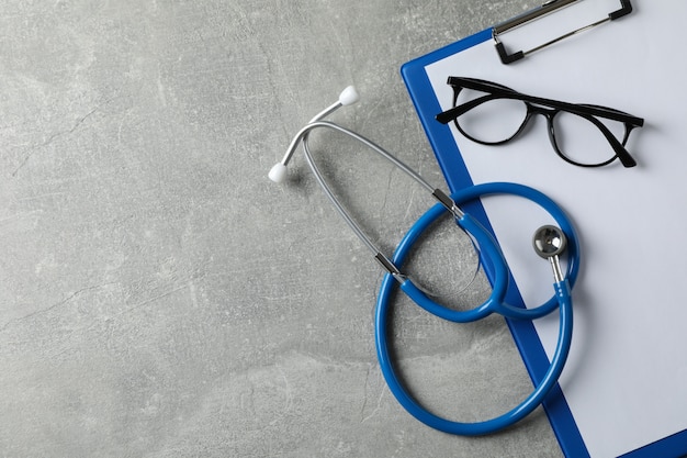 Stethoskop, Tablette und Brille auf grauem Hintergrund, Kopienraum