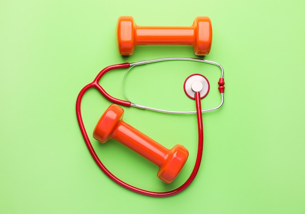 Stethoskop und Hanteln auf farbigem Hintergrund