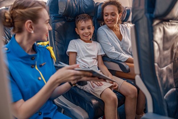 Stewardess, die versucht, ein Kind im Flugzeug zu unterhalten, indem sie ein Buch zum Lesen anbietet. Das Kabinenpersonal bietet Service für die Familie im Flugzeug. Luftverkehrs- und Tourismuskonzept
