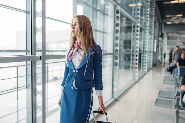 Stewardess mit Koffer im Wartezimmer des Flughafens