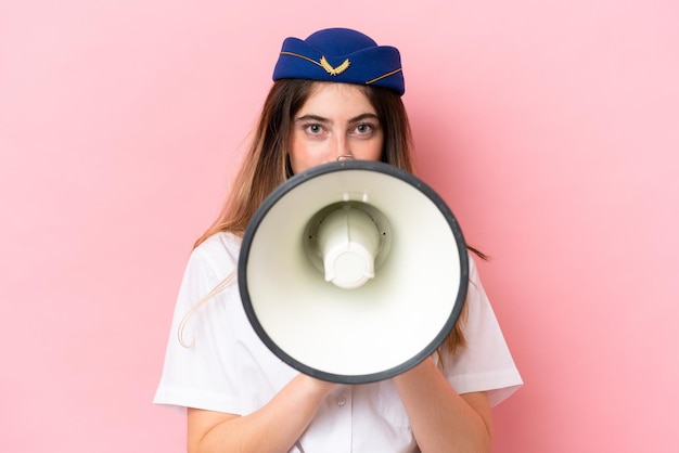 Stewardessa de avião mulher caucasiana isolada em fundo rosa gritando através de um megafone