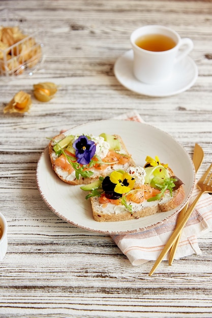 Ästhetische pescetarische Frühstückssandwiches mit gesalzenen essbaren Lachsblüten Avocado und Gurke Teetasse und Winterkirsche Atmosphärisches Mittagessen im Herbst