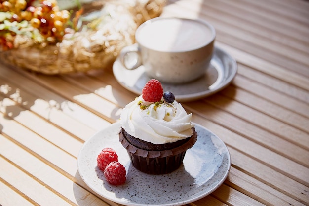 Ästhetischer französischer Beeren-Cupcake mit Cappuccino inmitten von Herbstdekoration unter sonnigen Lichtern Gemütliches Frühstück auf der Terrasse