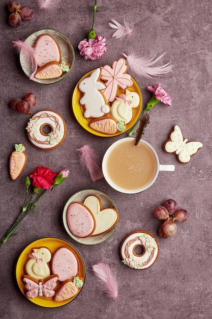 Ästhetischer Frühling Ostern Hintergrund komplette Kaffeetasse dekoriert glasierte Kekse Federn und Asterblumen flach gelegt Frühlingshintergrund