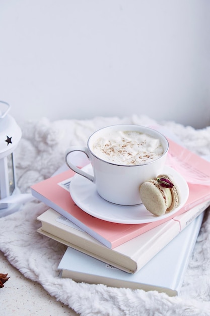 Ästhetisches Frühstück mit heißem Getränk mit schaumiger zarter Makrone auf den Büchern Süßes Dessert im gemütlichen Zuhause