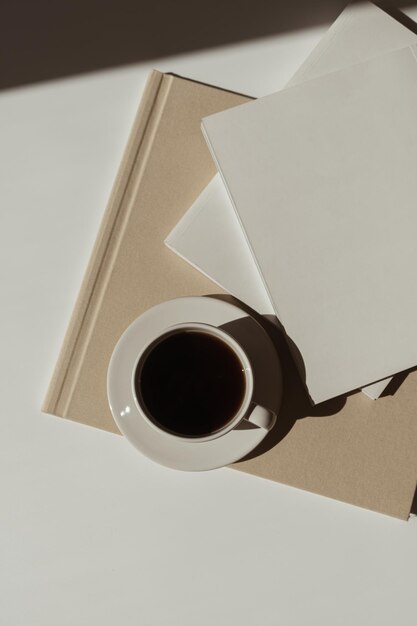 Ästhetisches, luxuriöses, böhmisches, minimalistisches Konzept Leeres Papierblatt Notizbuch Tasse Kaffeealbum Marmorsteintablett mit Sonnenlichtschatten Flache Ansicht von oben