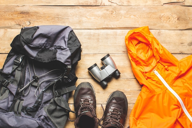 Stiefel für eine Spur, Jacke, Rucksack, Wanderausrüstung auf einem hölzernen Hintergrund. Das Konzept von Wandern, Tourismus, Camp, Bergen, Wald. Banner. Flache Lage, Draufsicht