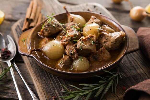 Stifado - delicioso ensopado de carne mediterrânea com bulbos de cebola, canela e temperos em uma caçarola, em uma mesa de madeira preta, vista de cima, close-up