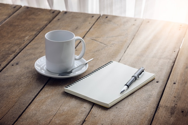 Stift auf Notizbuch mit Kaffeetasse auf hölzernem