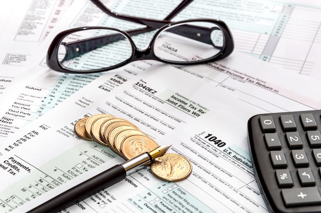 Stift, Brille, Taschenrechner und Münzen auf Steuerformularen. Unternehmenskonzept.